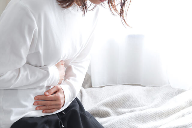 痛みを感じて手で腹を押さえている女性