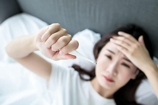 額に手を当てて体温計で熱を計っている女性